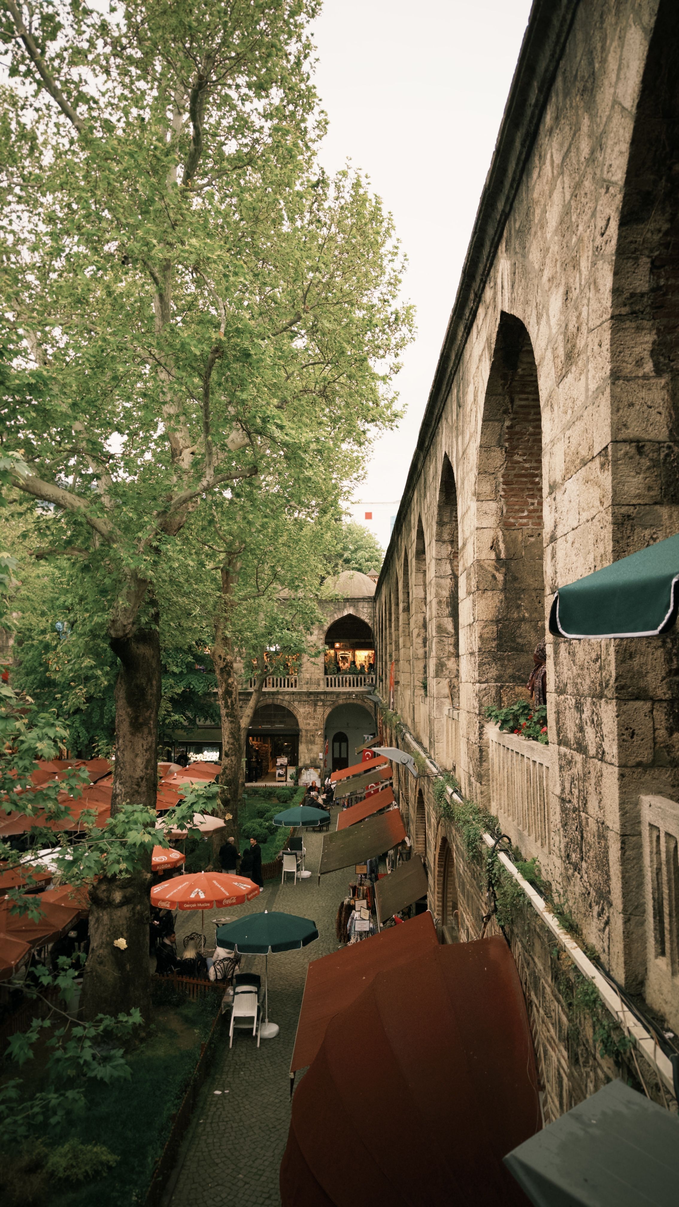 Charming outdoor cafe scene beside a historic stone architecture under lush trees.