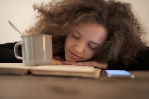 一名年轻女子在室内放松，将头靠在一本书上，旁边放着一个杯子