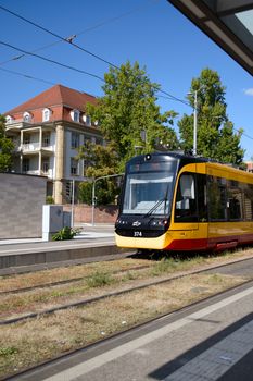 A modern yellow tram moves through a picturesque urban train station under a clear blue sky.