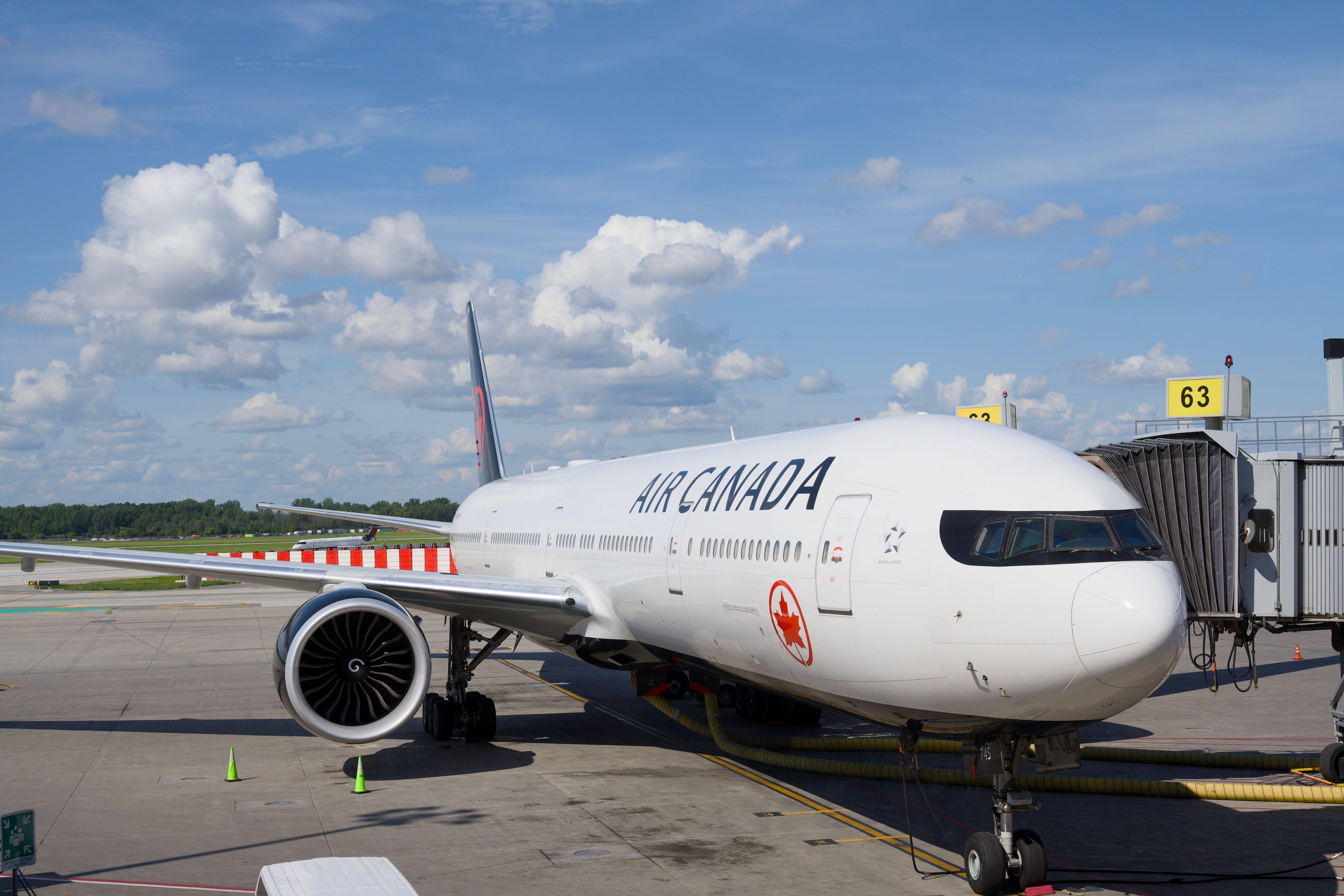 Air Canada Boeing 777 airplane parked at an airport gate under a clear blue sky.