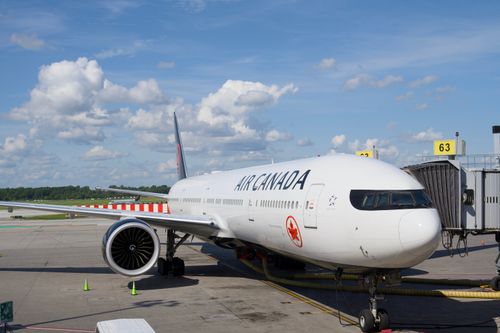 Free Air Canada Boeing 777 airplane parked at an airport gate under a clear blue sky. Stock Photo