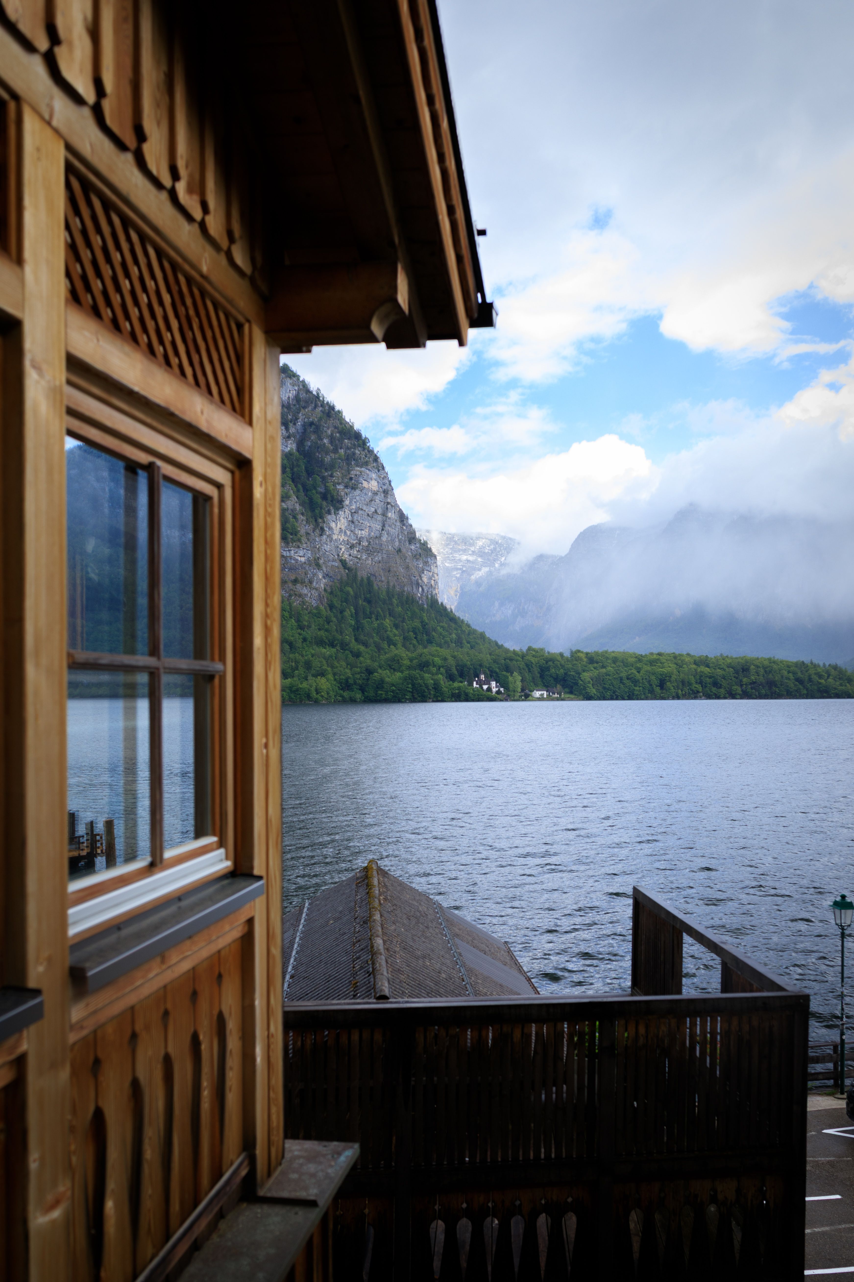 A tranquil alpine lake view with a wooden cabin and misty mountains in the background.