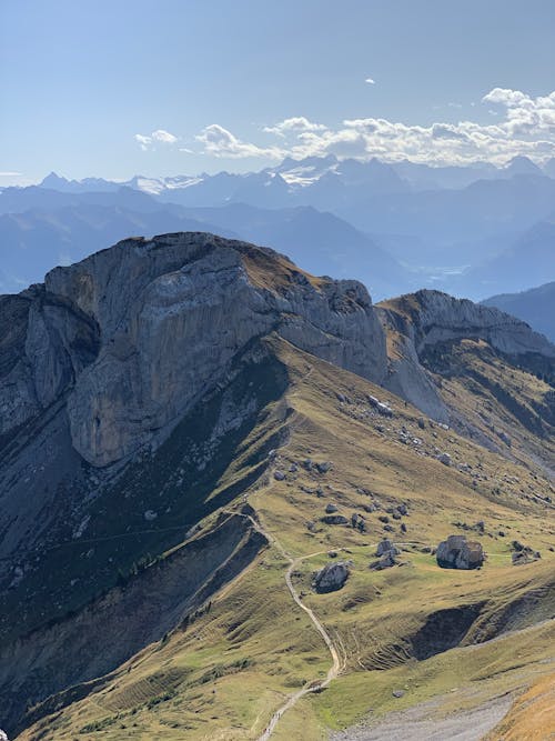 Picturesque rocky mountain range covered with grass highland against white clouds floating in blue sky