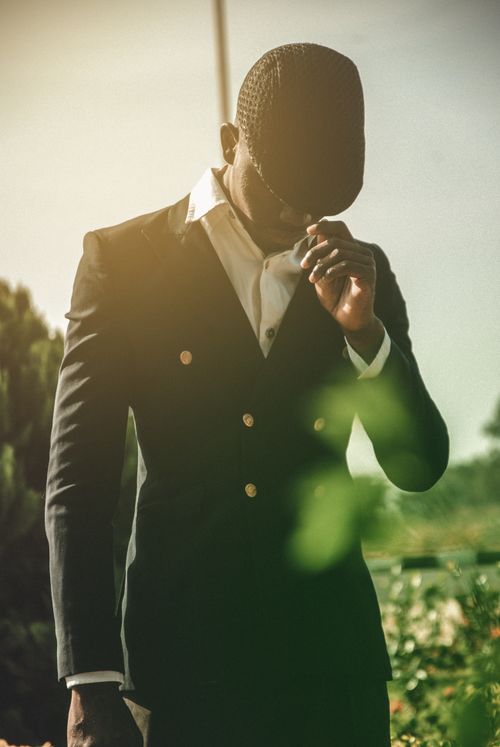 Free Fashionable man wearing a black suit and cap stands thoughtfully outdoors in daytime sunlight. Stock Photo