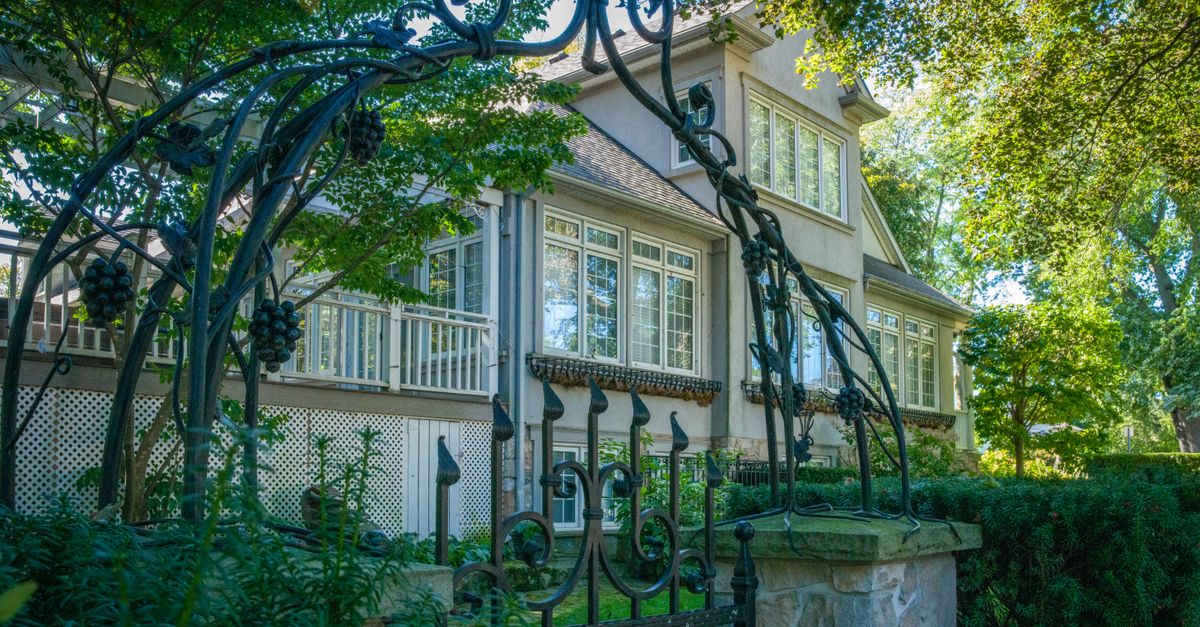 A charming house is visible through a beautifully designed wrought iron gate, surrounded by lush greenery.
