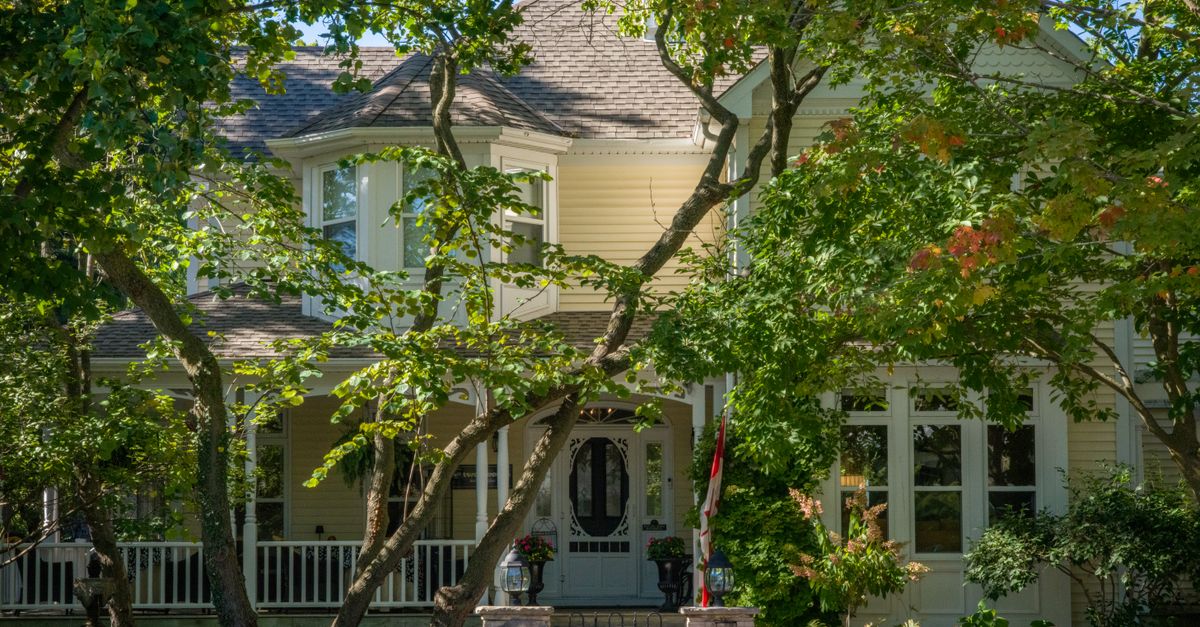 A picturesque Victorian house with lush greenery and vibrant trees in the front yard under a clear blue sky.