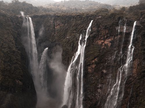 Free Dramatic waterfall plunges down lush, rocky cliffs in a stunning natural landscape. Stock Photo