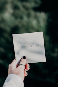 Close-up of a hand holding a note with an inspirational quote against a natural background.