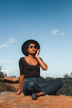 一位时尚女士坐在岩石上，享受着阳光明媚的户外时光