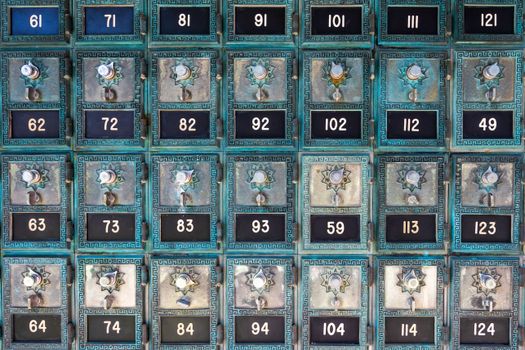 Rows of antique metal post office boxes with numbered dials and ornate designs.