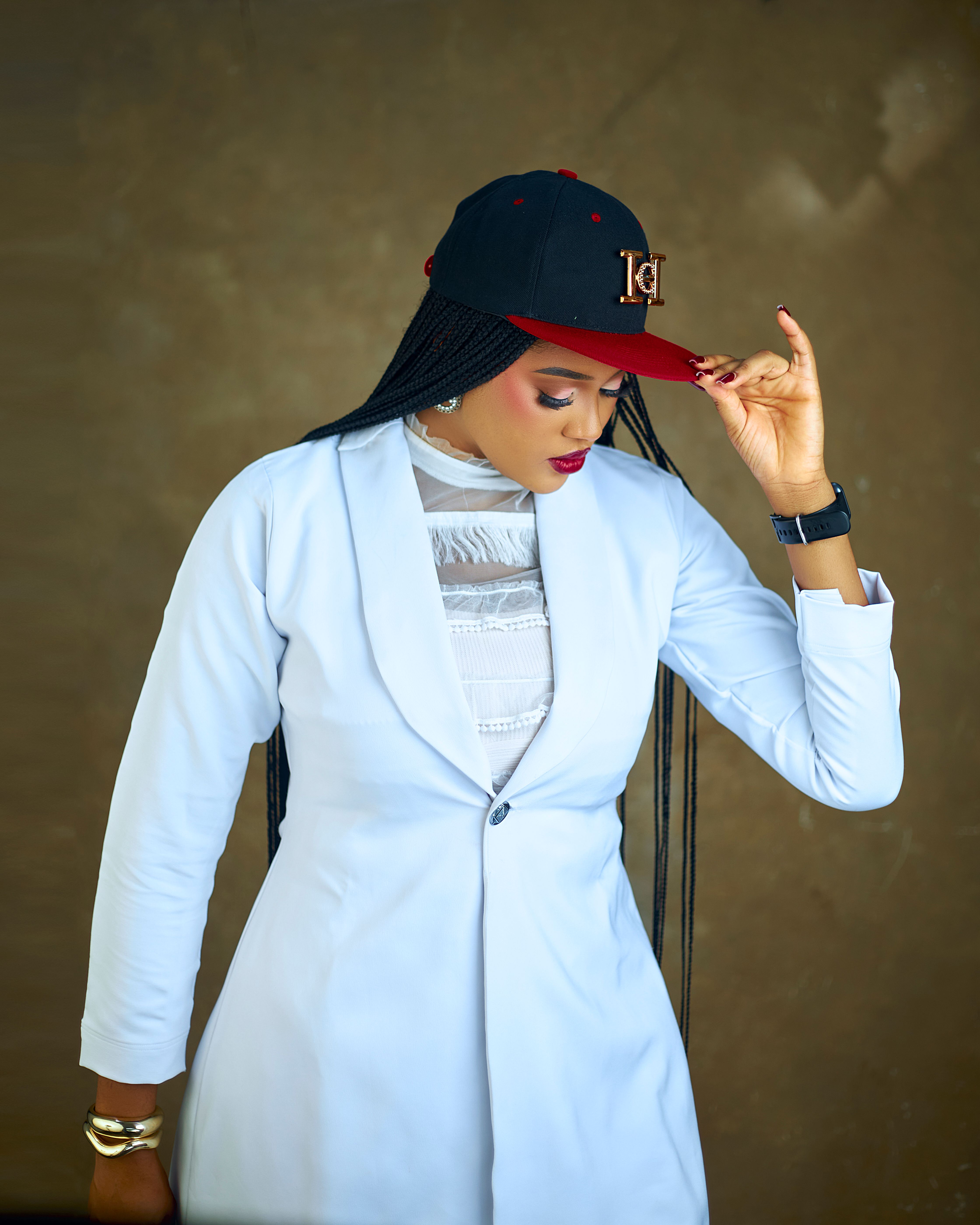 Fashionable African woman in a white blazer and cap striking a pose indoors.