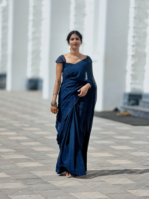 Free Portrait of an elegant woman in a navy saree walking past white columns outdoors. Stock Photo