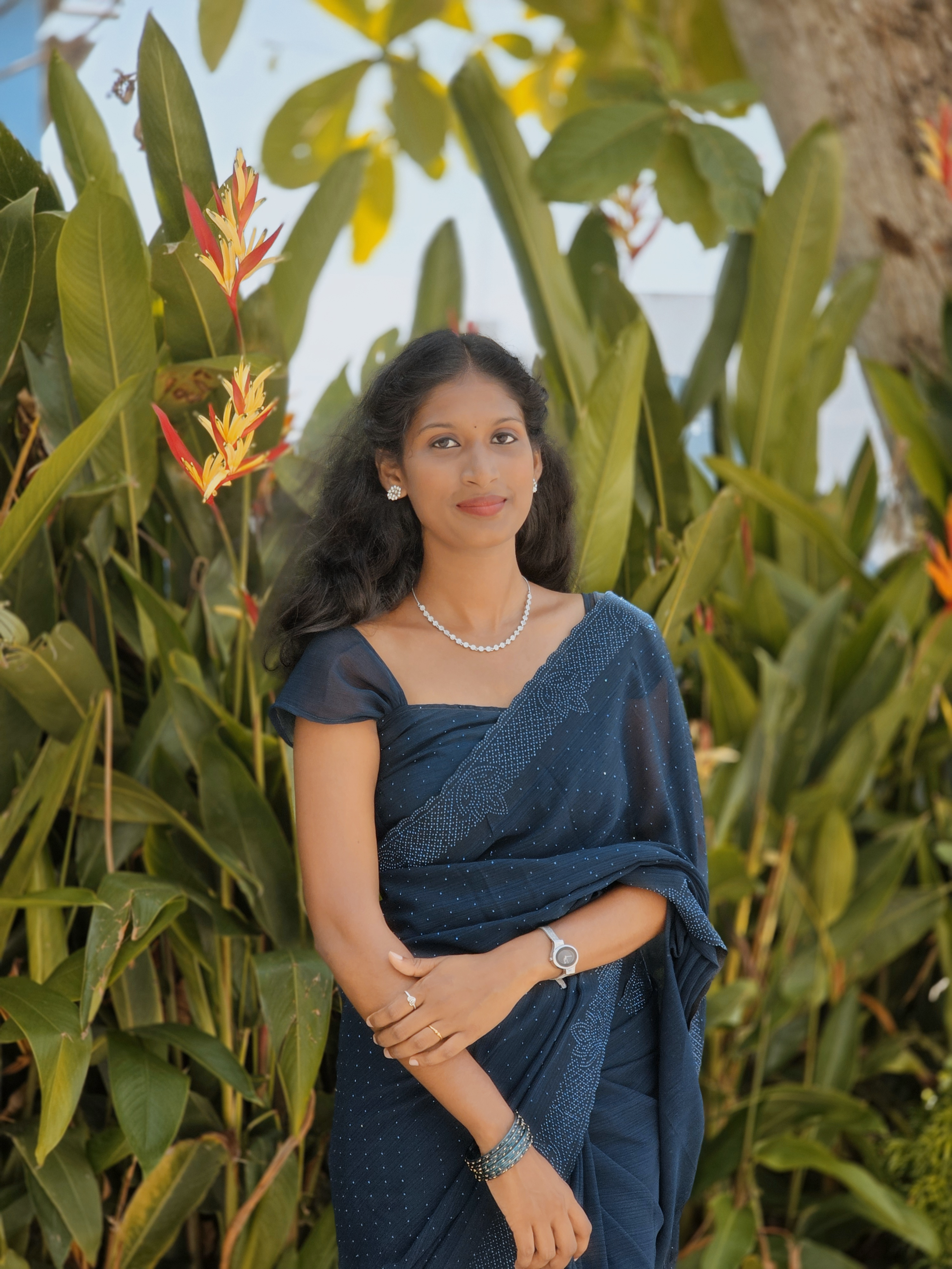 Elegant woman in traditional navy sari amidst lush greenery and tropical flowers.