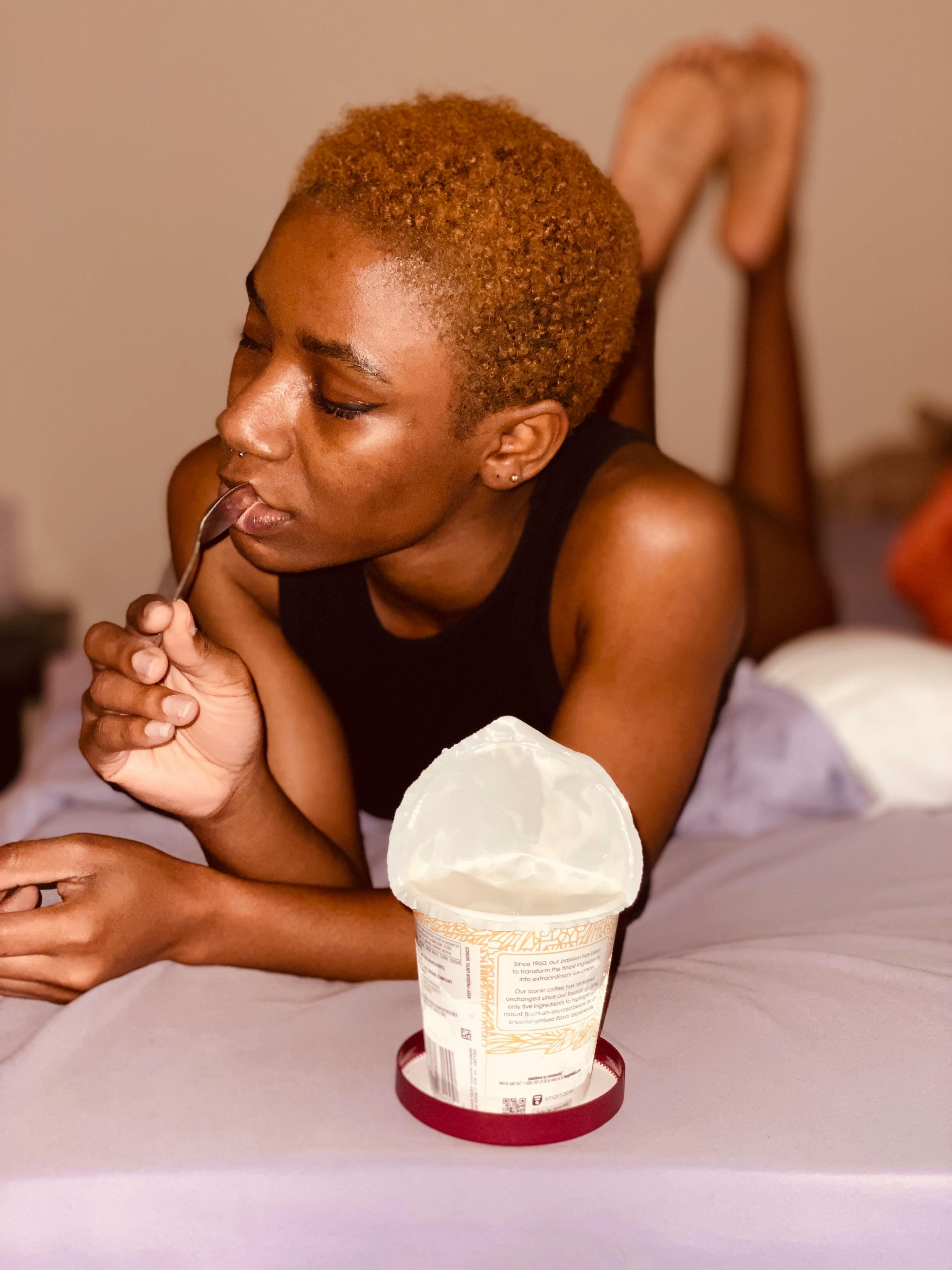 A woman enjoys ice cream on her bed, capturing a cozy and indulgent moment indoors.
