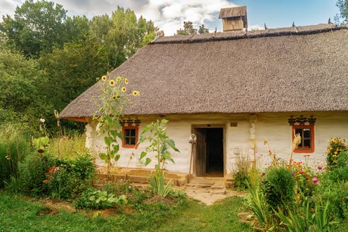 Free Image of a traditional thatched roof mud hut in Ukrainian countryside with lush garden. Stock Photo