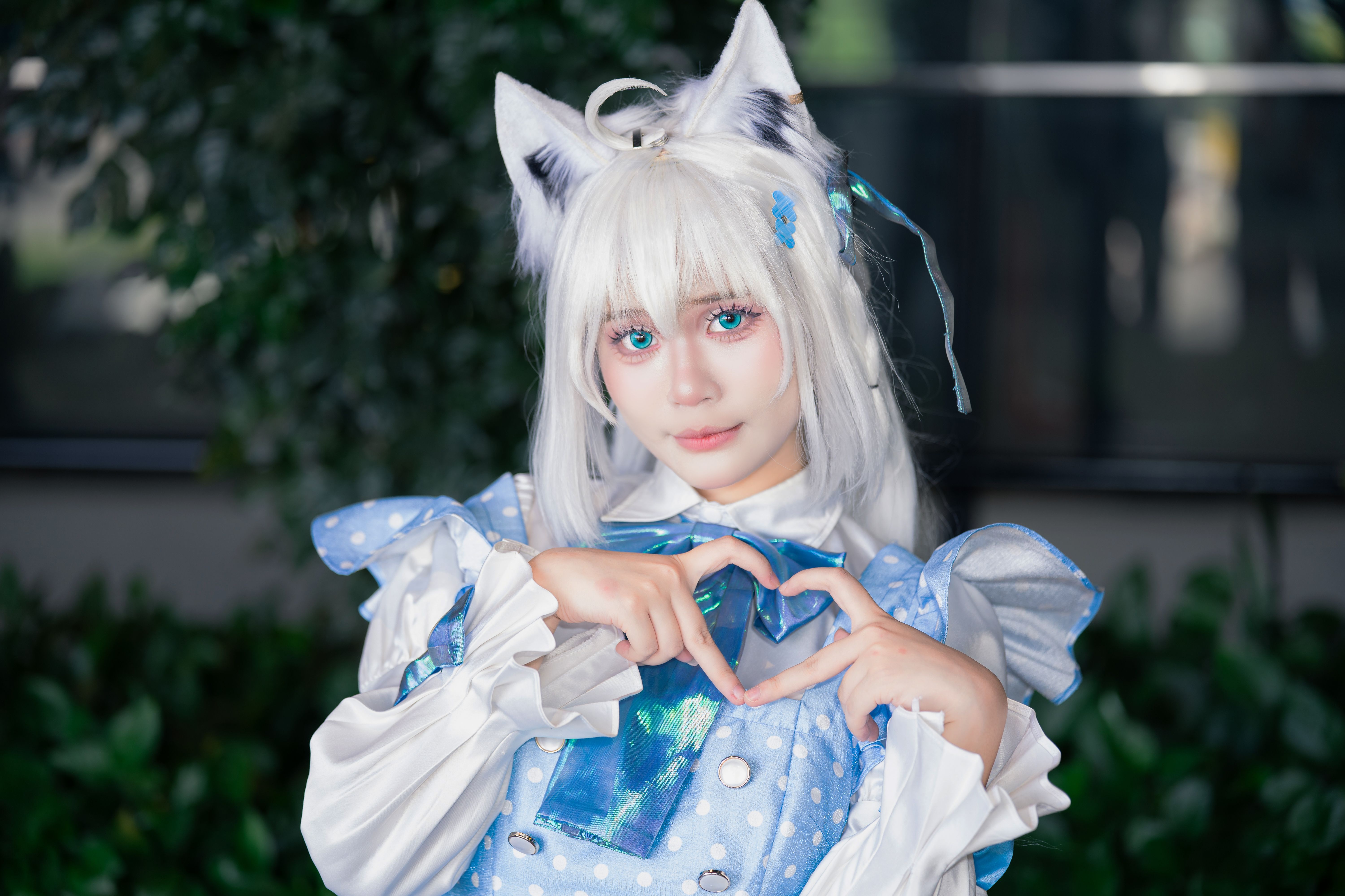 Charming young woman in kawaii cosplay with cat ears, making a heart gesture.