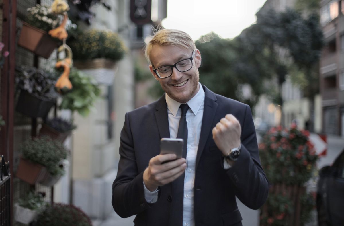 A cheerful professional pumping his fist while looking at his phone outdoors