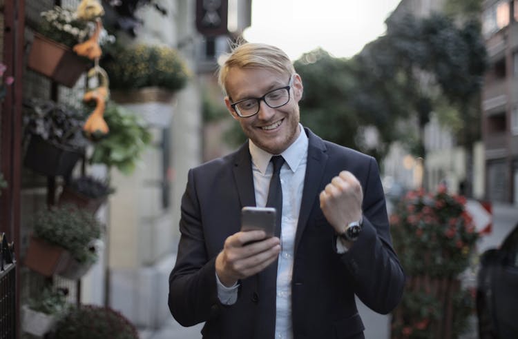 Cheerful Male Manager With Mobile Phone Standing Near Flower Shop In Street