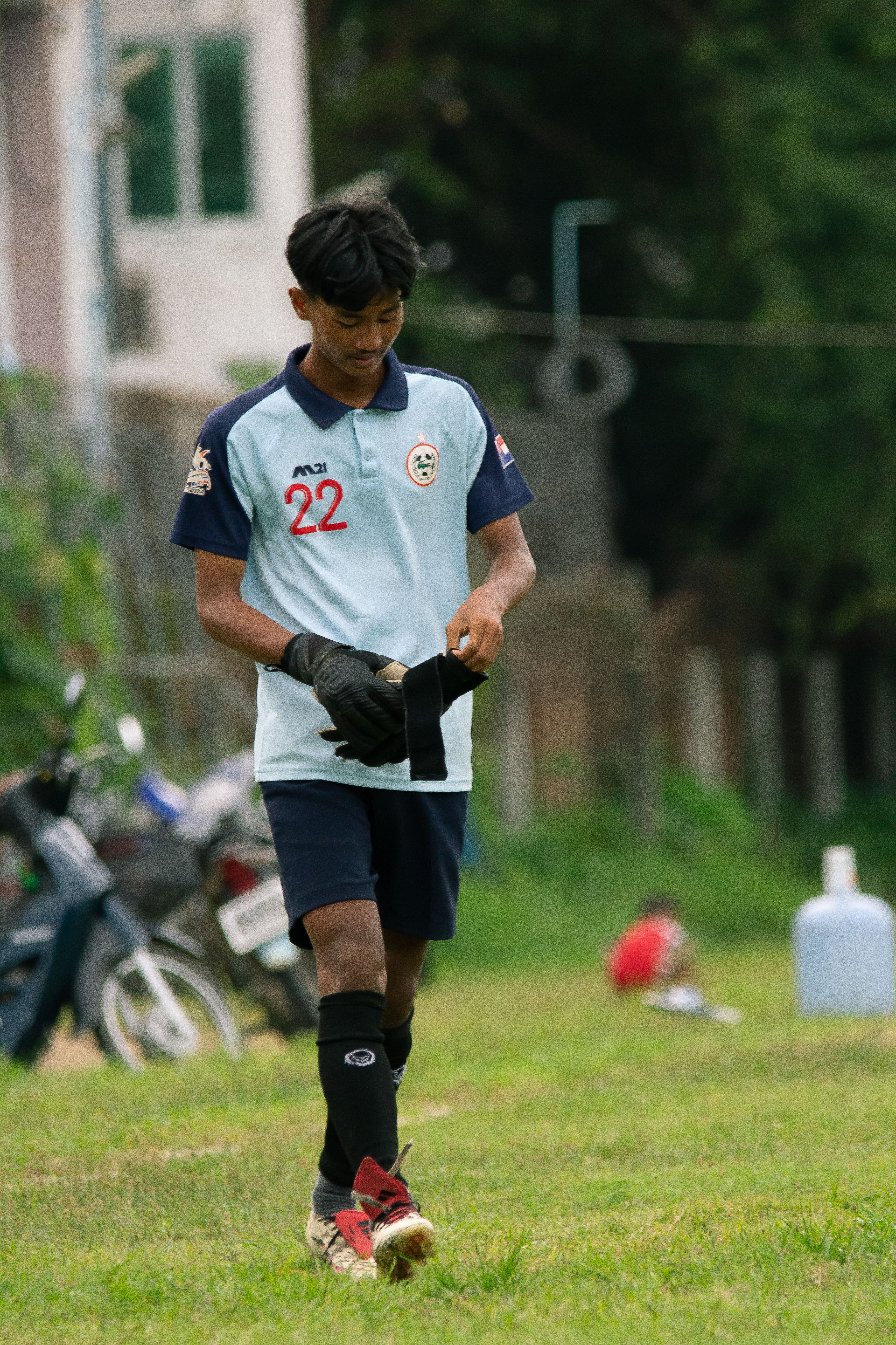 A teenage football player getting ready on a field in Myawaddy, Myanmar, wearing a team jersey.