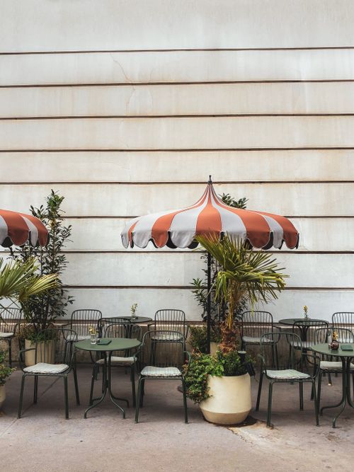 Free Cozy Viennese outdoor cafe with striped umbrellas and greenery. Ideal for urban relaxation. Stock Photo