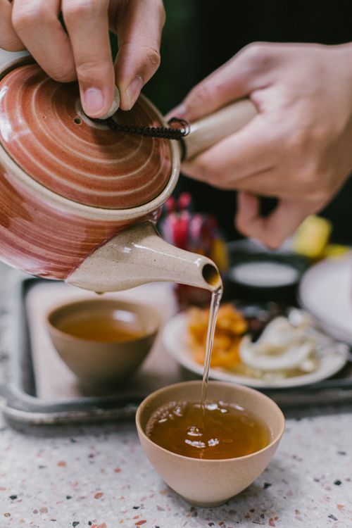 Free A serene moment pouring tea from a red ceramic teapot into a cup, capturing the essence of tranquility. Stock Photo