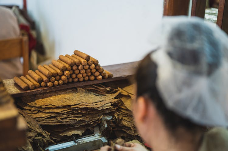 Faceless Worker Peeling Tobacco Leaves Near Heap Of Sausages In Factory