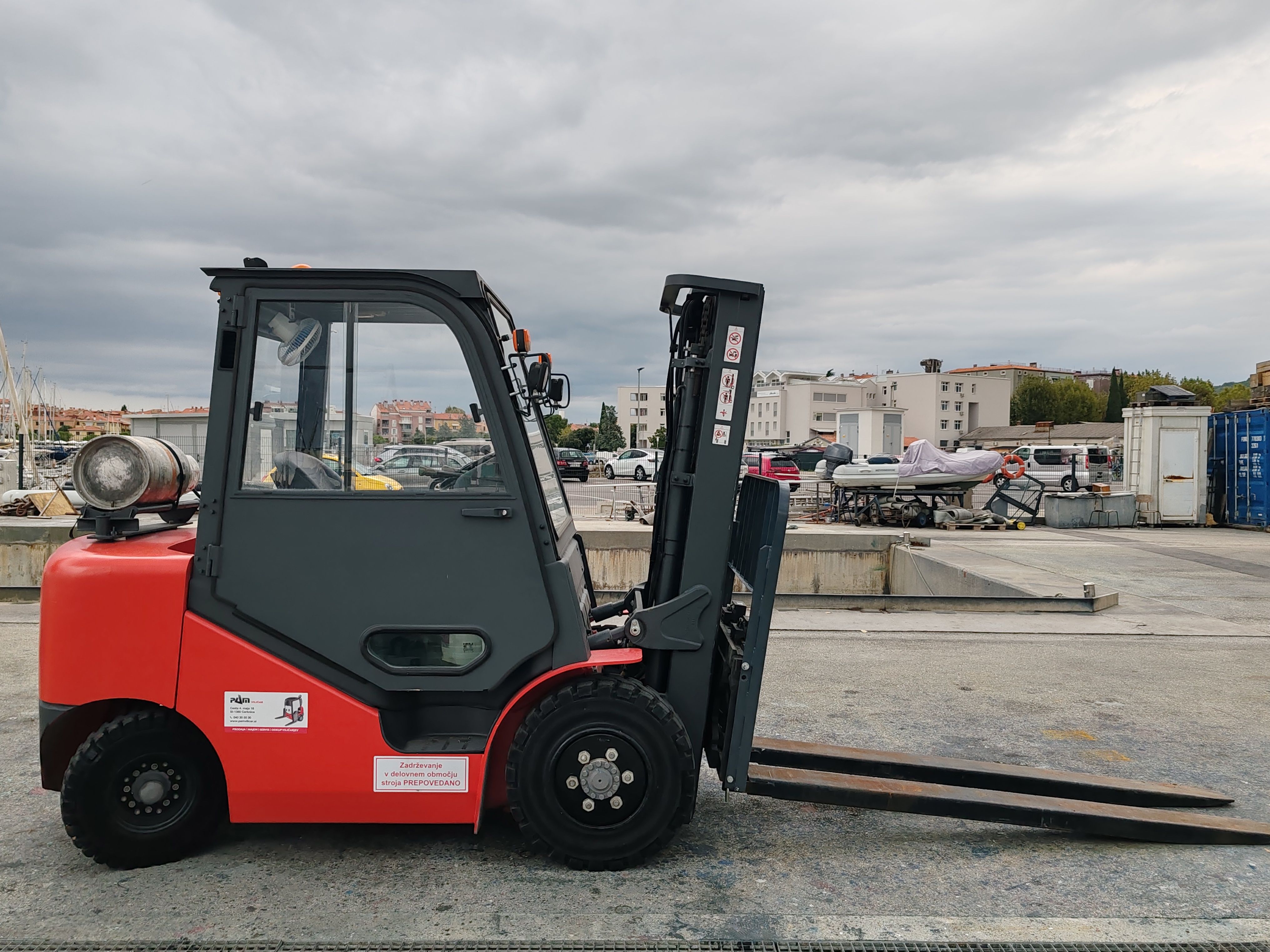 Red industrial forklift parked in a dockyard with urban background.