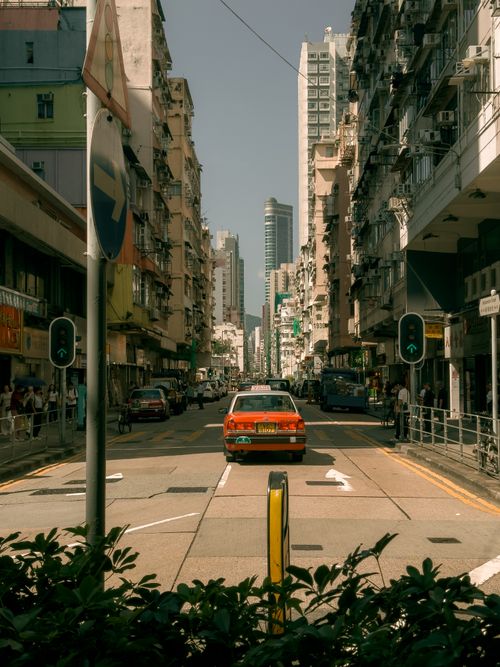Free Vibrant Hong Kong street view featuring a classic red taxi amidst bustling city life on a sunny day. Stock Photo