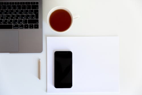 Free Workplace with smartphone placed on white paper with cup of tea aside near laptop and pencil Stock Photo