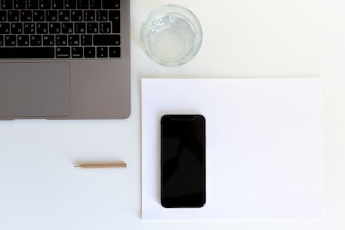 From above of smartphone placed on white paper with laptop and glass of water preparing for working day in modern workplace