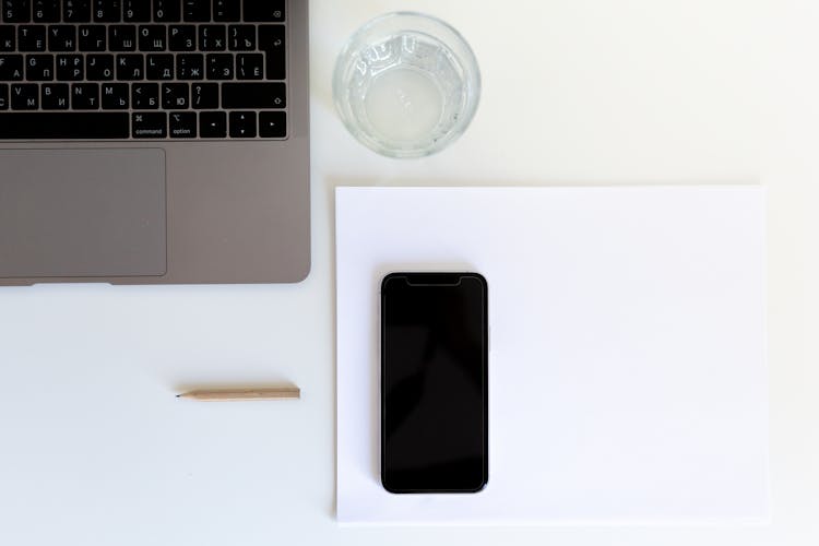 Netbook Keyboard And Glass Of Water Arranged On Table Near Cellphone On Empty Paper And Pencil