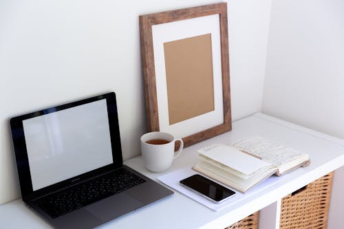 Free From above of empty frame placed near laptop daily planner and cup of hot drink and mobile phone in between in light room Stock Photo