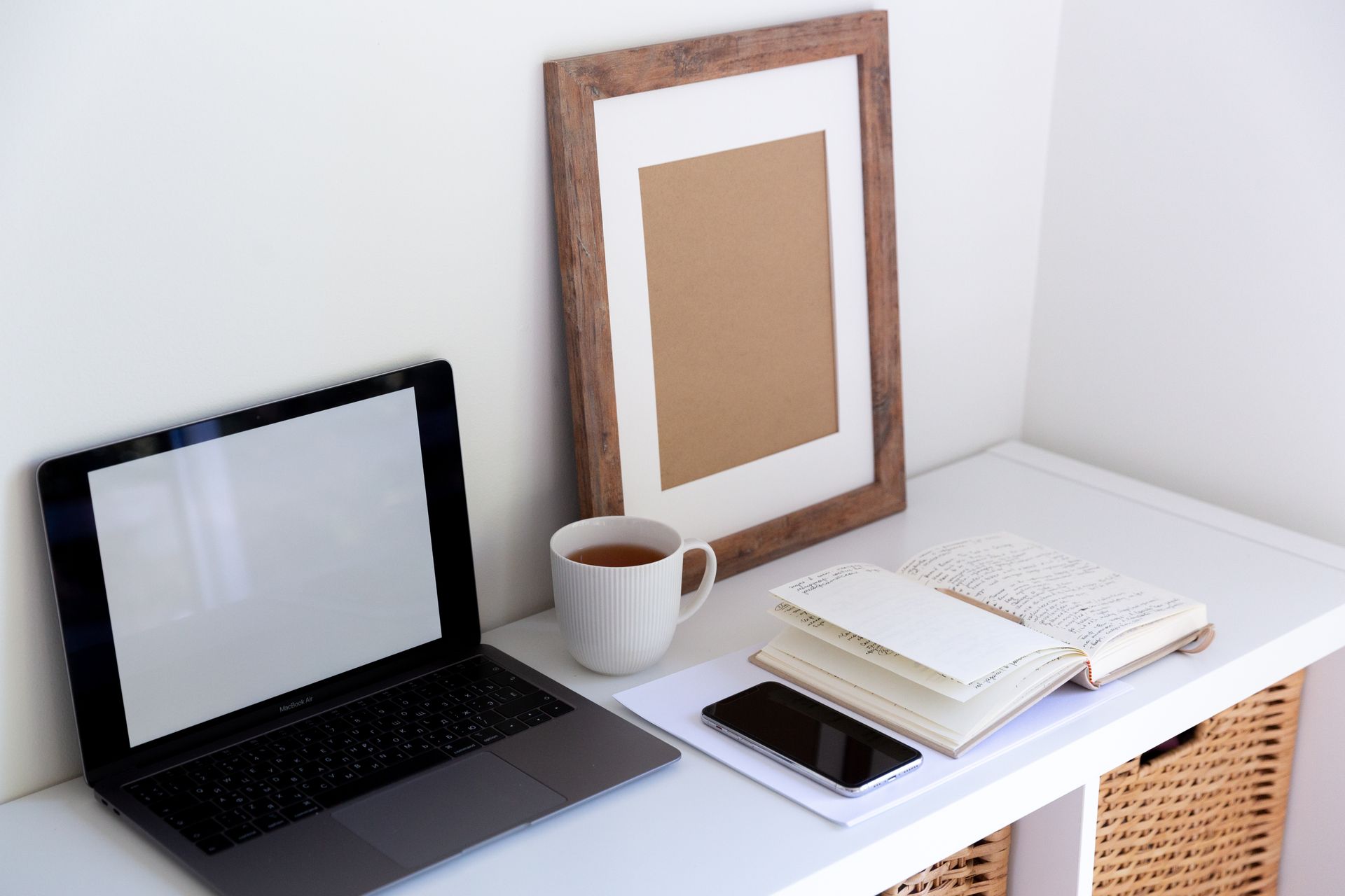 From above of empty frame placed near laptop daily planner and cup of hot drink and mobile phone in between in light room