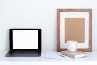 Minimalistic workplace with laptop and empty frame with office attributes during coffee break