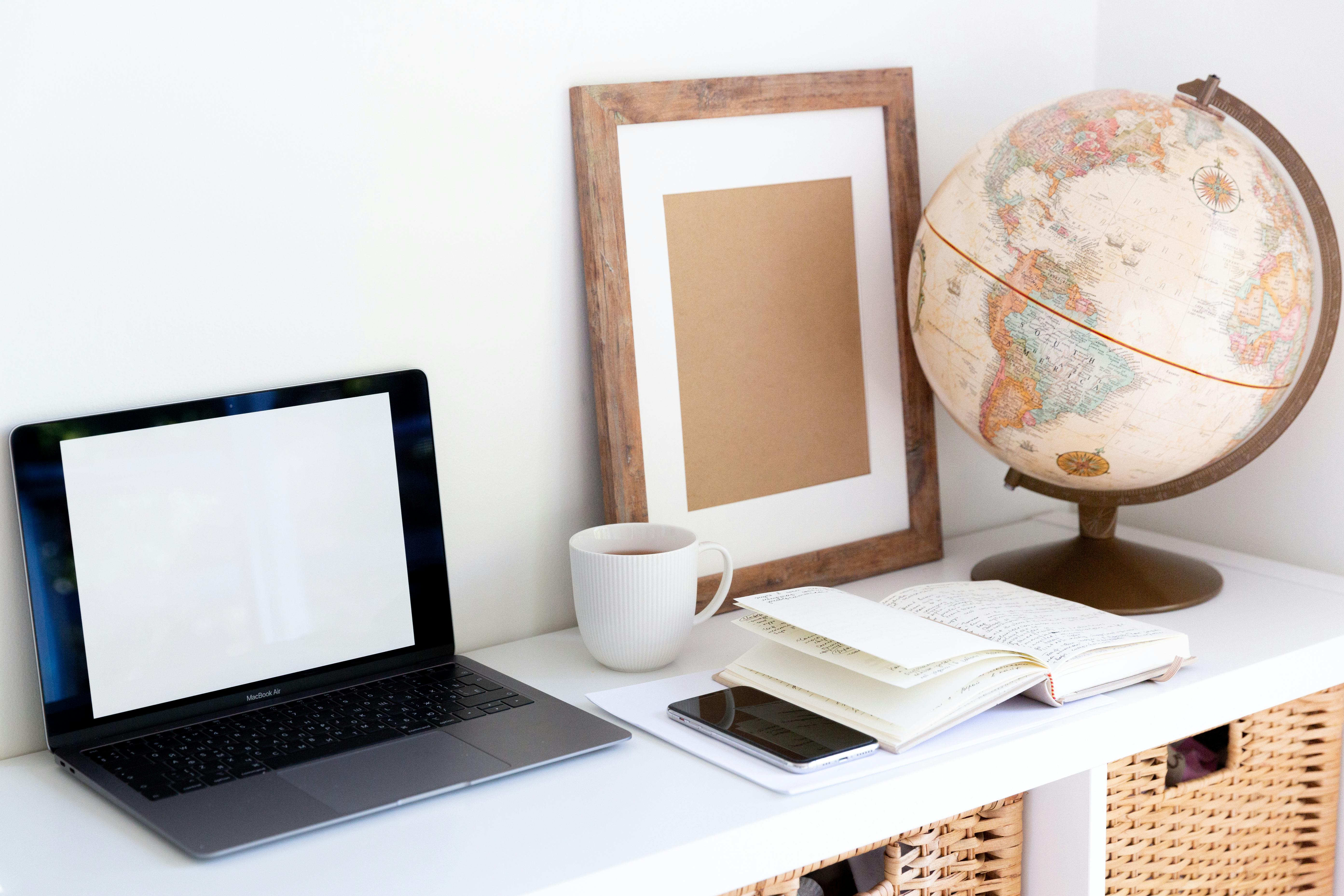 creative workspace with vintage globe near empty frame planner and modern gadgets