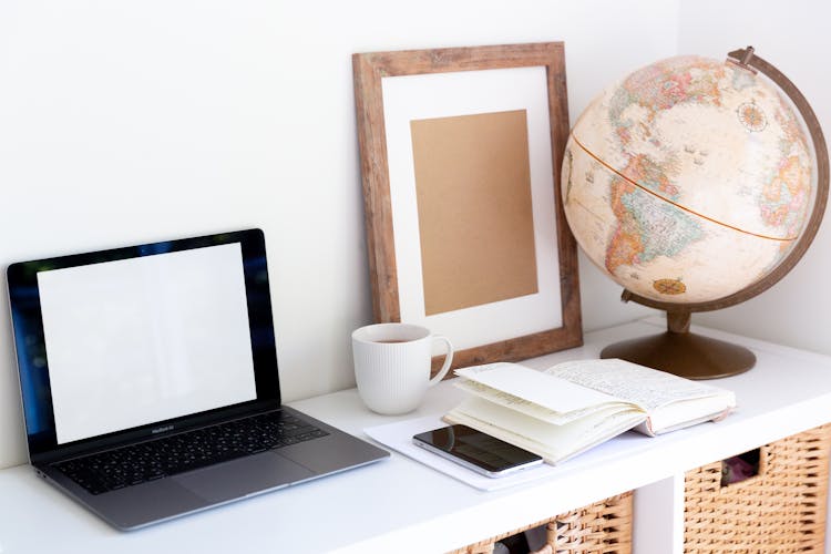 Creative Workspace With Vintage Globe Near Empty Frame Planner And Modern Gadgets