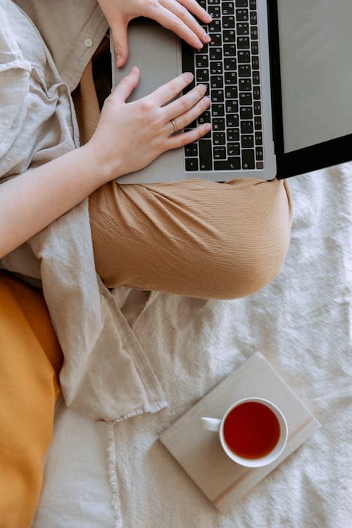 Free Anonymous woman in casual clothes sitting on sofa and browsing laptop with blank screen while working on project on bed Stock Photo