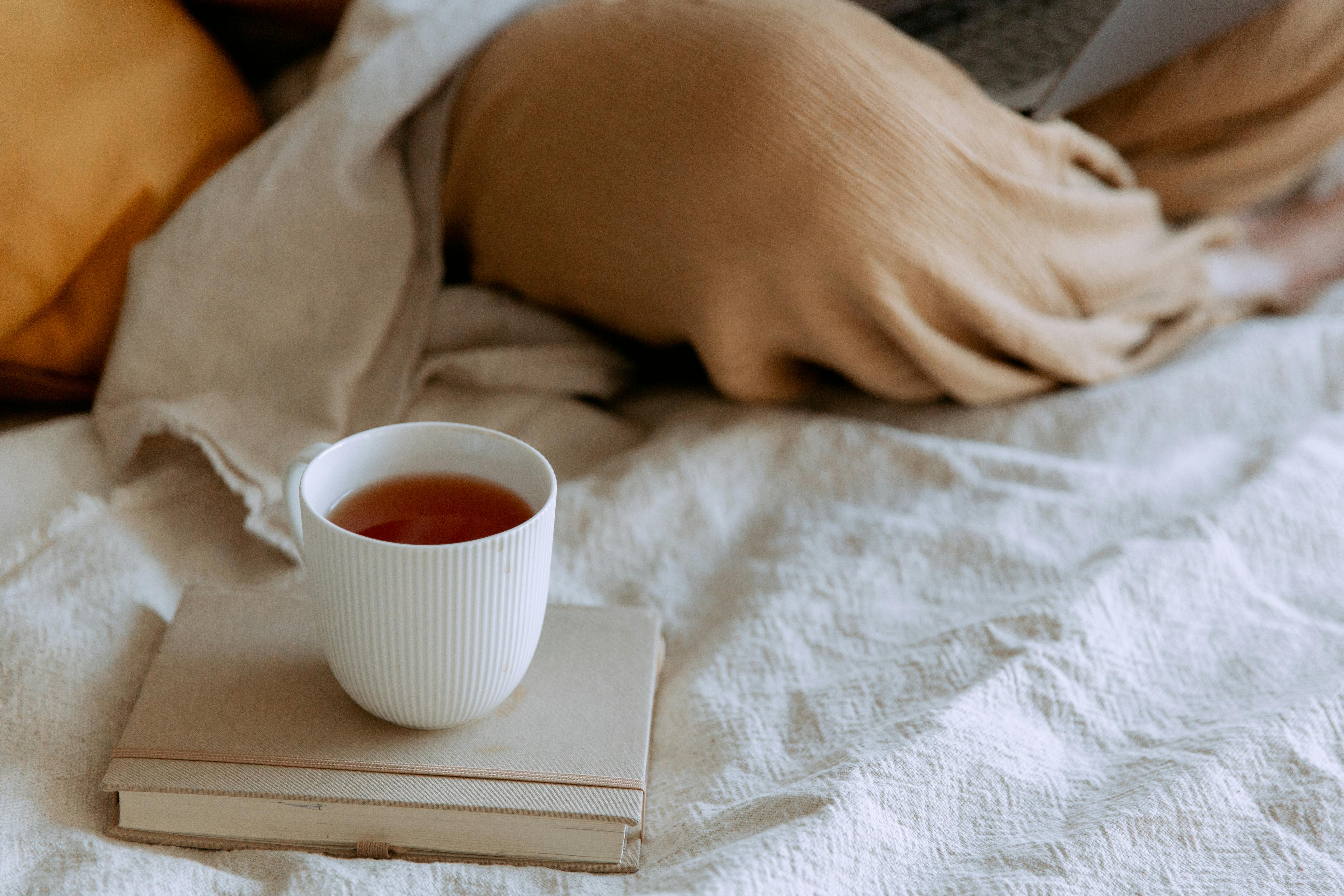 cup of hot tea on notebook near working person on laptop in bedroom