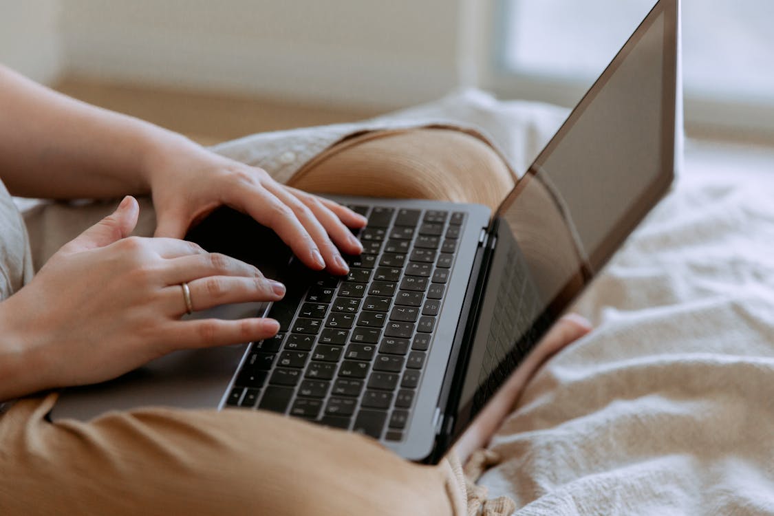Free Faceless woman using laptop while sitting on bed Stock Photo