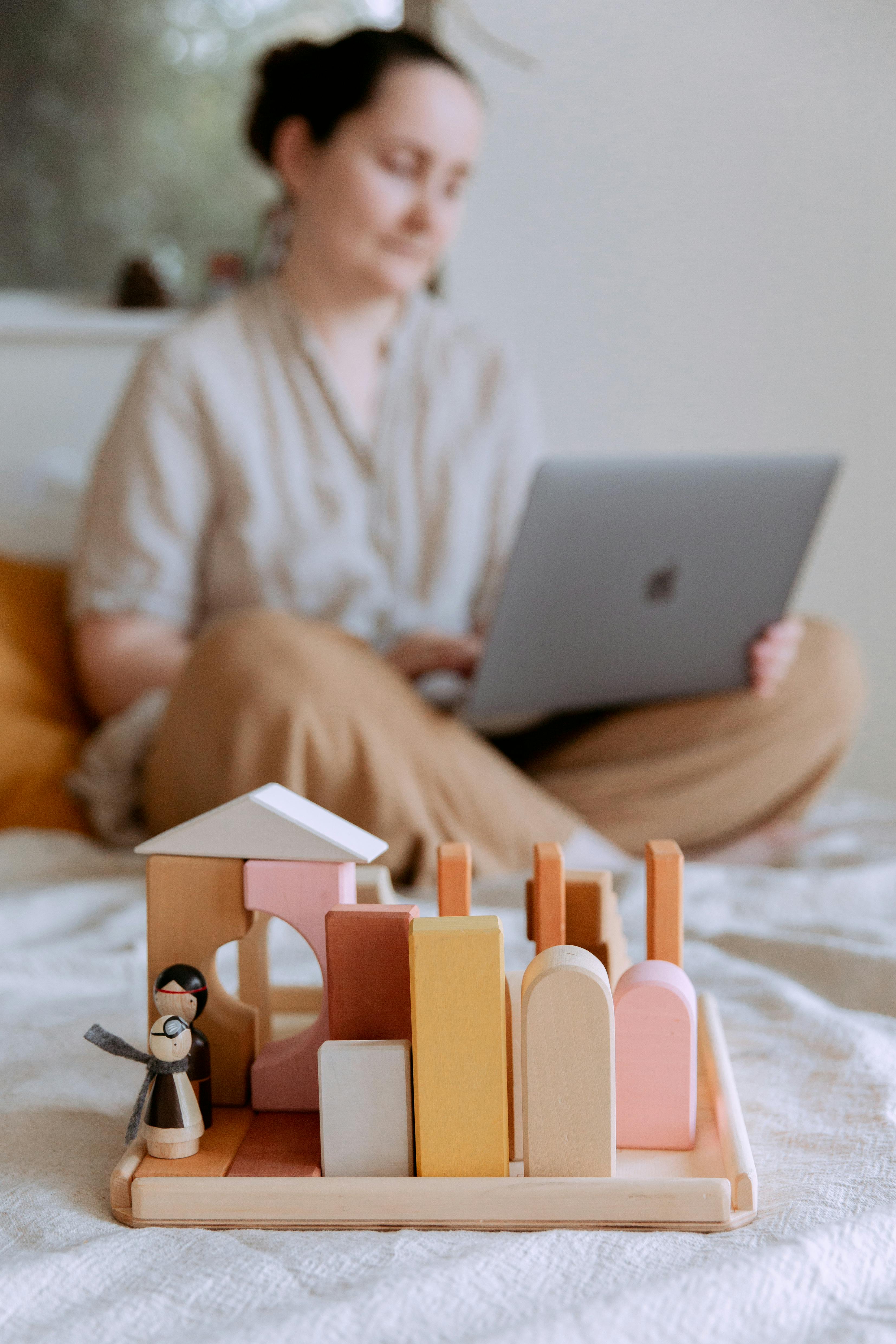 wooden blocks and toys standing on bed and focused woman with laptop on background