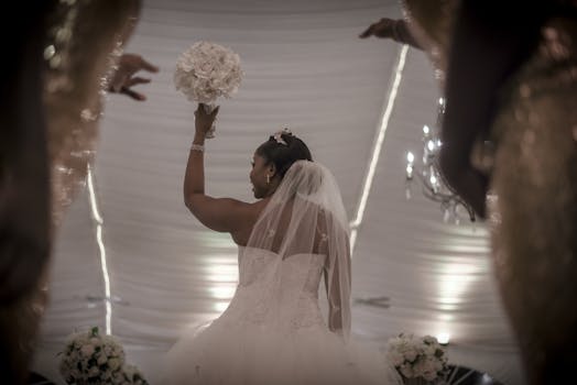 A bride holds up her bouquet triumphantly during an indoor wedding ceremony, capturing elegance and celebration.