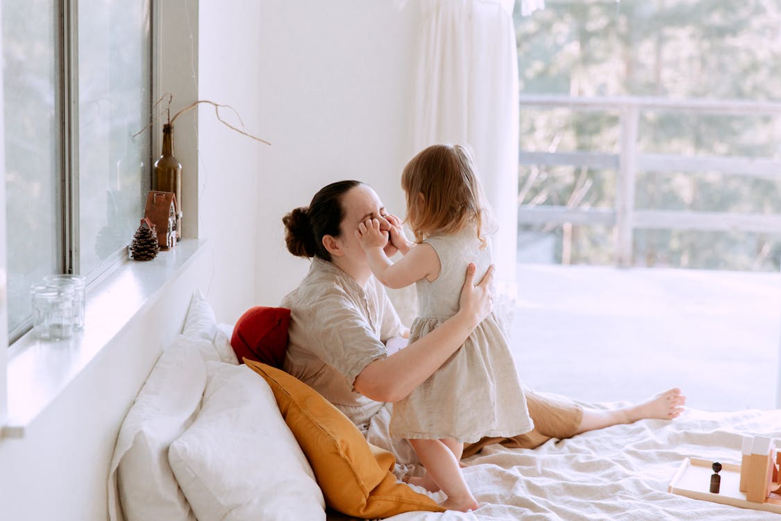 Mother and daughter having fun in bedroom while spending time together at home