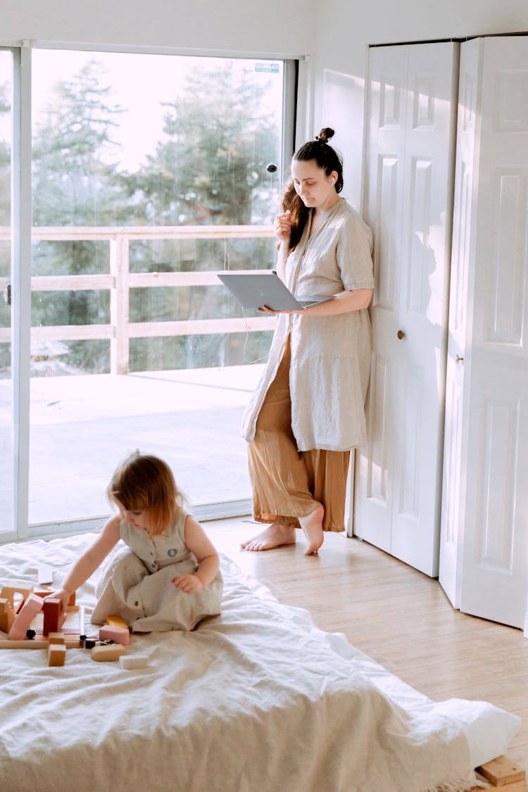 Woman Using Laptop In Bedroom With Daughter