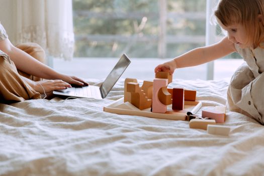 Crop mother and daughter sitting on bed while using laptop