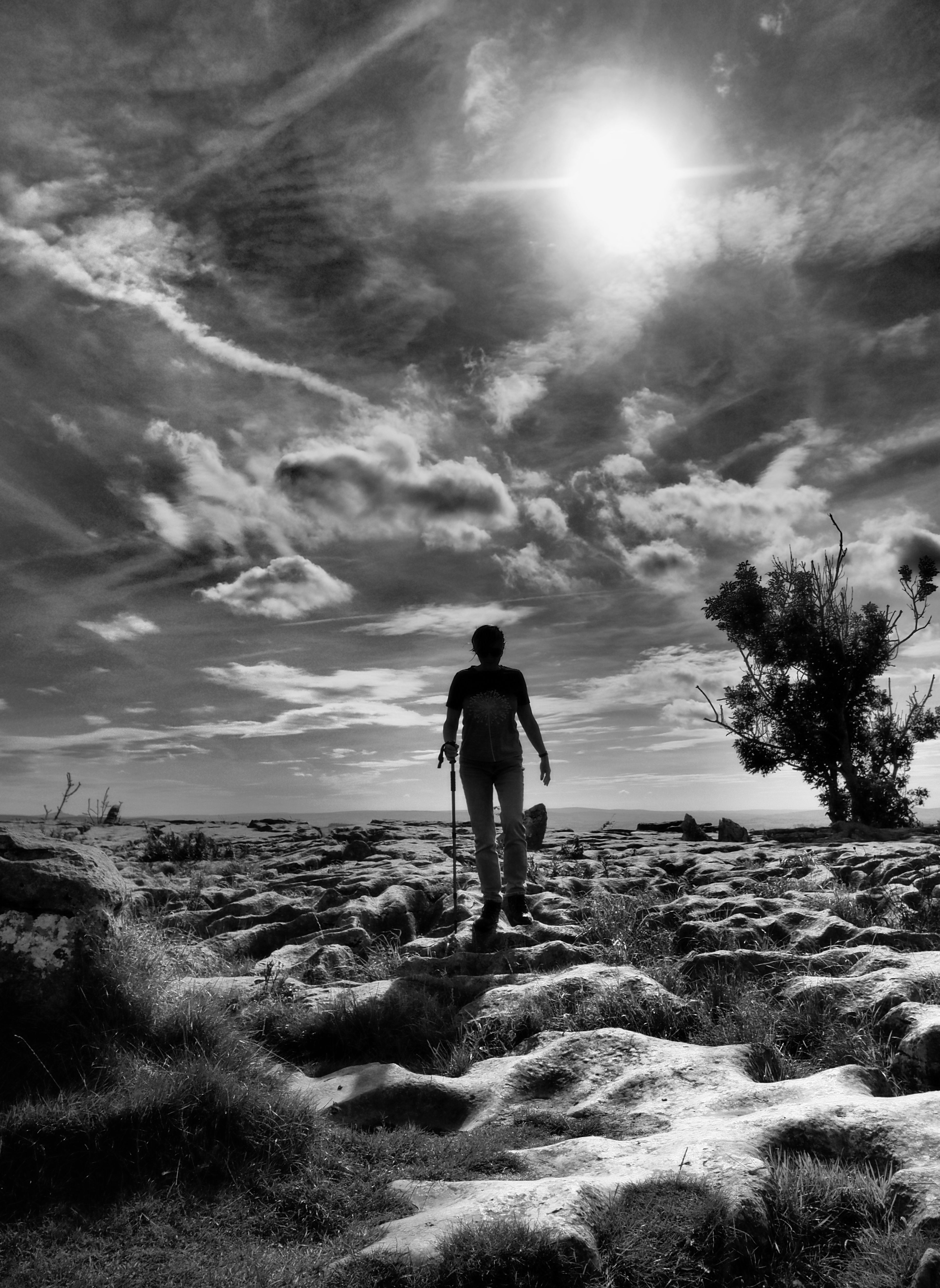 Silhouette of a hiker walking on rugged terrain in Malham, England, under a dramatic sky.