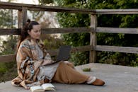 下午，一位戴着披肩、正在打盹的远程办公女员工坐在围栏露台上，旁边摊开着一本书，一边看着上网本的屏幕