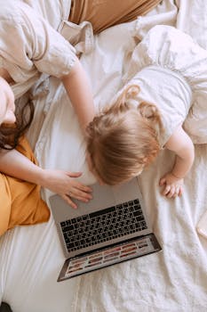 母亲和孩子舒适地坐在床上，一起用笔记本电脑共享屏幕时光