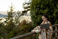 一位裹着披肩的妇女在阳台上用笔记本电脑，享受着宁静的户外环境