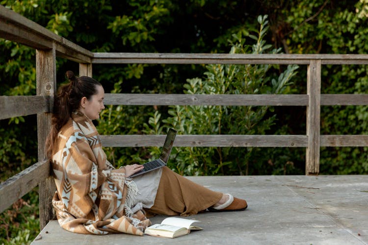 Adult Focused Female Blogger Sitting On Veranda With Laptop