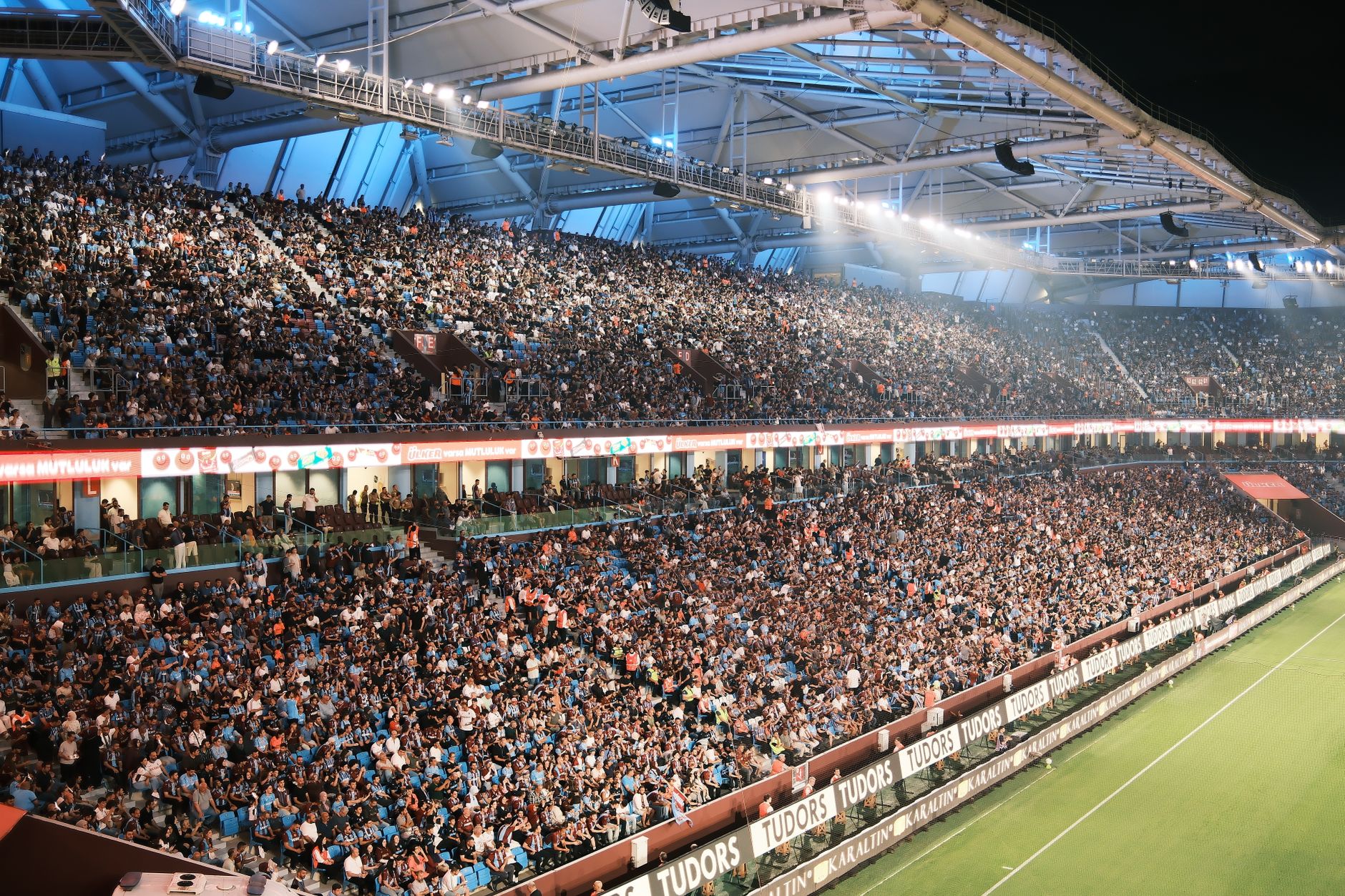 A packed football stadium illuminated at dusk, supporters holding national flags before a World Cup match